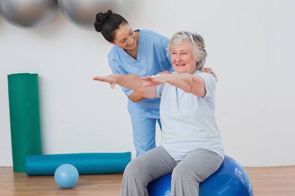 Happy instructor assisting senior woman in exercising at gym